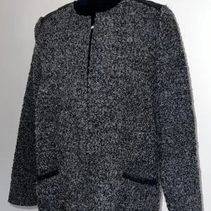 Grå lång kappa med läderdetaljer - Lång grå kappa i mjukt tyg med stiliga läderdetaljer som ger en modern touch. Denna kappa är både elegant och bekväm. Det finns en liten repa på axeln, men den är knappt synlig och påverkar inte det övergripande utseendet.