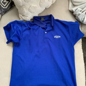 Blå pikétröja från Callaway Golf - Säljer en blå pikétröja från Callaway Golf. Tröjan har korta ärmar och en klassisk krage med knappar. Perfekt för golfbanan eller en avslappnad dag ute.