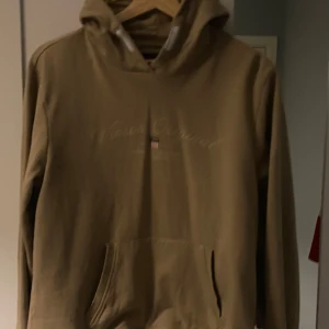Beige hoodie från Vinson - Säljer en beige hoodie från Vinson med en diskret logga på bröstet. Tröjan har en klassisk känguruficka och en bekväm huva. Perfekt för en avslappnad stil.