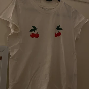 Vit t-shirt med körsbärstryck från Gina Tricot - Säljer en söt vit t-shirt från Gina Tricot med ett körsbärstryck på bröstet. Perfekt för en avslappnad stil. 🍒