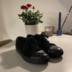 Arigato Cap Toe Sneakers - Snygga svarta sneakers från Axel Arigato med en stilren design. Skorna har en svart sula och snörning framtill. Läder på tån och svart mocka runt. Ser ut som Lanvins!! Perfekta för en minimalistisk look. Nypris över 2200 kr!!!! Skriv till mig vid minsta fråga!!