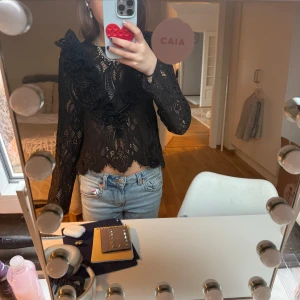 Zara topp - Säljer en elegant svart spetsblus med vackra volangdetaljer. Blusen har långa ärmar och en fin struktur som ger en lyxig känsla. Perfekt för att lyfta vilken outfit som helst.