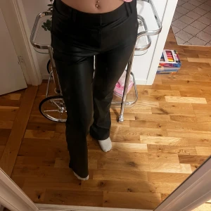 Svarta byxor från Zara - Snygga svarta byxor från Zara i skinnimitation. De har en tight passform och är högmidjade, vilket ger en stilren look. Perfekta för att lyfta vilken outfit som helst.