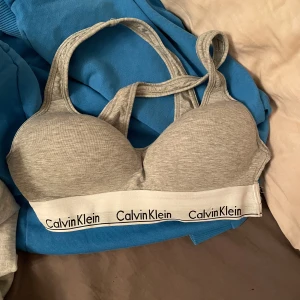 Grå bh från Calvin Klein - Säljer en grå bh från Calvin Klein med bred resår och logga. Den har en bekväm passform med brottarrygg och är tillverkad i mjukt bomullsmaterial. Även lite push up! Denna är i storlek XS sista bilder ser man litet slitage den har! 