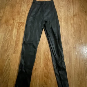 Svarta högmidjade byxor - Snygga svarta högmidjade byxor i ett stilrent och tight snitt. Perfekta för en chic look med en dragkedja framtill. Passar utmärkt till olika tillfällen och kan enkelt matchas med olika toppar.