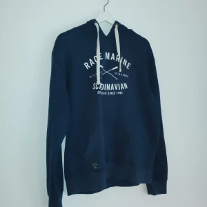 Mörkblå hoodie från Race Marine - Säljer en snygg mörkblå hoodie från Race Marine med vit text på framsidan. Den har en justerbar huva med vita snören och en stor ficka framtill. Perfekt för en avslappnad stil.