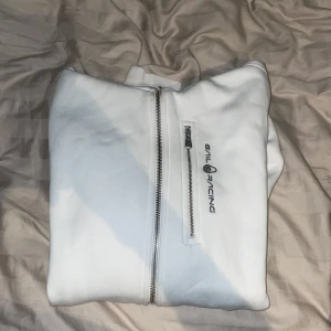 Vit hoodie från Sail Racing - Säljer en stilren vit hoodie från Sail Racing med dragkedja framtill. Tröjan har långa ärmar och en praktisk bröstficka med dragkedja. Perfekt för en avslappnad stil. Helt ny är tröjan, använd max 2 gånger fick den under min växt period där den inte passar längre. Den ser helt ny ut som man ser på bilderna och på insidan är den fortfarande helt len och skön. Säljer den pga att jag är i behov av pengar. Pris kan alltid pratas skriv visa meddelande eller skicka pris förslag.