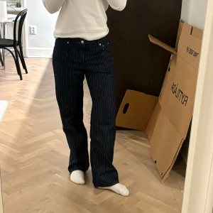 Randiga jeans från Claire Rose x NA-KD - Snygga mörkblå jeans med vita ränder från Claire Rose’s kollektion med NA-KD. Byxorna har en klassisk femficksdesign och stängs med dragkedja och knapp. Sparsamt använda. Storlek 36.