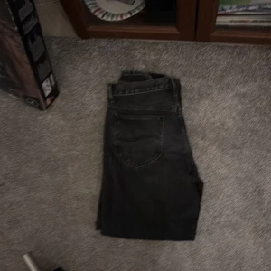 Svarta jeans från Lee - Snygga svarta jeans från Lee med klassisk femficksdesign. De har en rak passform och är perfekta för en stilren look. Jeansen har en knappgylf med Lee-logga och är tillverkade i slitstarkt denim.