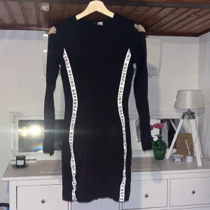 Figursmickrande klänning från divide - Snygg svart klänning med långa ärmar och textdetaljer längs sidorna som ger en fin timglasform. Klänningen har en tight passform. Ärmarna har ett band av mesh. Strl 36. Knappt använd