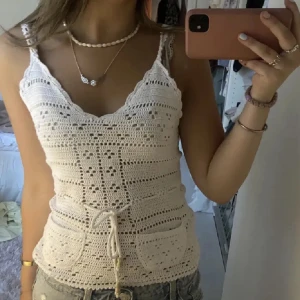 Vit virkad linnetopp - Säljer en söt vit virkad linnetopp med knytning och fickor framtill