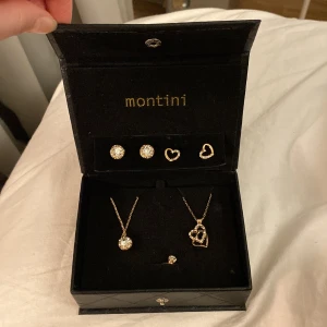 Smyckeset från Montini med hjärtan och stenar - Elegant smyckeset från Montini innehållande två par örhängen, ett halsband med en gnistrande sten och ett halsband med ett hjärthänge och sist en fin ring med sten. Setet kommer i en stilren svart ask med quiltat mönster. Perfekt för att lägga till en touch av glamour.
