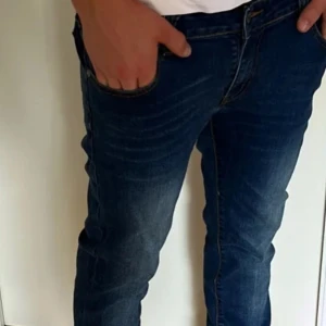 Mörkblå jeans med broderade bakfickor - Snygga mörkblå jeans får nudie med en klassisk slim fit design och broderade detaljer på bakfickorna. Jeansen har en normal passform och är perfekta för en avslappnad stil.