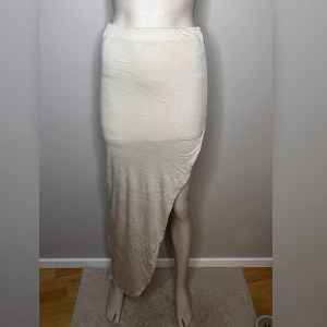 Beige kjol från BikBok - Beige kjol från BikBok i en asymmetrisk design med slits. Kjolen har en tight passform med en underkjol. Tillverkad i ett mjukt och stretchigt material.