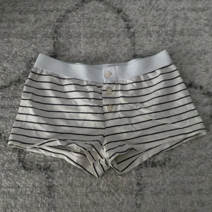 Randiga shorts från Brandy Melville - Säljer ett par vita shorts med svarta ränder från Brandy Melville. De har en bekväm elastisk midja och tre knappar framtill. Inga tecken på användning!