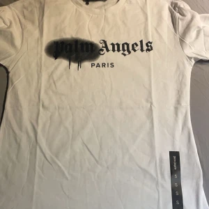 Vit t-shirt från Palm Angels - Säljer en vit t-shirt från Palm Angels med ett coolt tryck i svart på framsidan. T-shirten har en rund hals och korta ärmar. Perfekt för en avslappnad stil med en touch av streetwear.