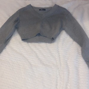 Grå croppad tröja med v-ringning - Säljer en stilren grå croppad tröja med v-ringning. Tröjan har långa ärmar och är ribbad vid ärmslut och nederkant. 