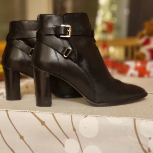 Svarta boots med klack och spännen - Snygga svarta boots i skinn med hög klack och dekorativa spännen. Perfekta för en stilren look. De har en spetsig tå och är tillverkade i ett elegant material.