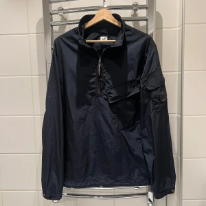 Marinblå vindjacka från C.P. Company - Snygg marinblå vindjacka från C.P. Company med halv dragkedja och ficka på bröstet och armen. Pris kan diskuteras