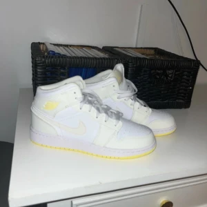 Nike Air Jordans i vitt och gult - Snygga Nike Air Jordans i vitt med gula detaljer. Skorna har en klassisk hög design med snörning och en bekväm sula. Perfekta för en stilren look.