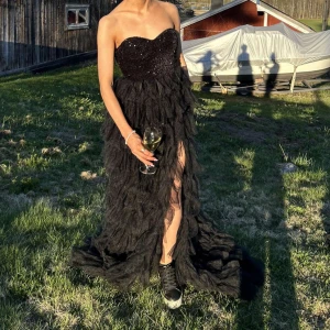 Svart axelbandslös klänning - Elegant svart axelbandslös klänning med glittrig överdel och volangdetaljer. Klänningen har en slits framtill. Perfekt för en kväll ute eller en speciell tillställning. Använd en gång🤍nypris ca 800 kr