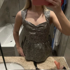 Glittrig topp med öppen rygg - Snygg glittrig topp med en unik öppen ryggdesign. Toppen har breda axelband och en peplumliknande nederdel som ger en fin siluett. Perfekt för en festlig kväll! Pris kan diskuteras!🪩💕