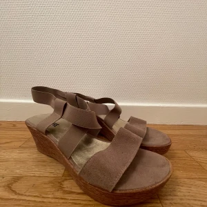 Kilklack beige. Storlek 39/40 - Kilklack i beige. Band med stretch kring foten och mocka imitation framme vid tårna. Märkta storlek 40, men mer som storlek 39. (Jag har 39 i vanliga fall och de passar mig perfekt). Från yttersta tån till hälen mäter dem 25,5 cm. Mycket fint skick, se bilderna. Stretch i banden över foten så passar bra.