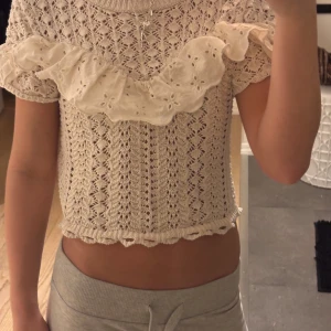 Beige stickad topp med volangdetaljer - Säljer en söt beige stickad topp från Zara med vackra volangdetaljer över axlarna. Toppen har ett fint mönster och korta ärmar. Passar bra till både jeans och kjol. 🌟