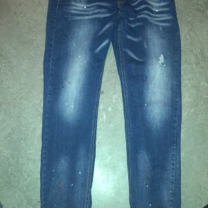 Blå jeans med slitna detaljer - Snygga blå jeans med en cool sliten look och färgstänk. De har en klassisk femficksdesign och en bekväm passform. Perfekta för en avslappnad stil.