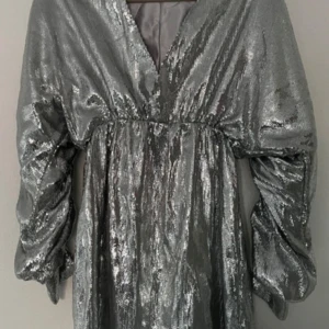 Glittrig silverklänning från Linn Ahlborg x NA-KD - Säljer en glittrig silverklänning från Linn Ahlborg x NA-KD. Klänningen har en v-ringad design och långa ärmar, perfekt för att glänsa på festen. Den har en elegant passform som framhäver figuren. Perfekt för dig som vill sticka ut! ✨