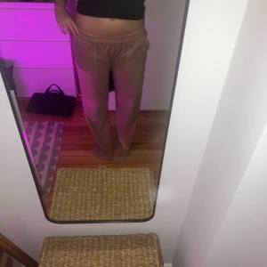 Beige mjukisbyxor från Juicy Couture - Snygga beige mjukisbyxor från Juicy Couture i ett mjukt och glansigt material. Byxorna har en bekväm resårmidja med snörning och två fickor framtill. Perfekta för en avkopplande fredagskväll! Dom har inga defekter. Jag är 164 cm i referens.