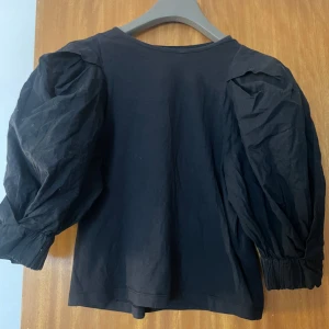 Svart blus med puffärmar - Snygg svart blus med puffiga långa ärmar. Perfekt för en stilren look med en touch av volym. Tillverkad i ett mjukt material som ger en bekväm passform.