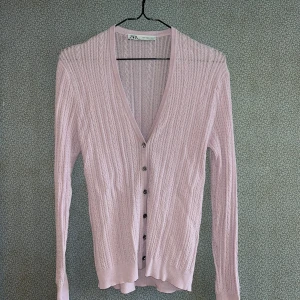 Ljusrosa stickad kofta från Zara - Säljer en ljusrosa stickad kofta från Zara med v-ringning och dekorativa knappar. Koftan har ett fint flätmönster och långa ärmar. Perfekt för en stilren look. 🌸