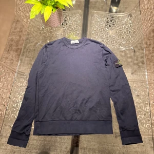 Mörkblå tröja från Stone Island - Säljer en stilren mörkblå tröja från Stone Island. Tröjan har långa ärmar och en rund halsringning. Den ikoniska logotypen är placerad på ärmen. Perfekt för en avslappnad och trendig look.