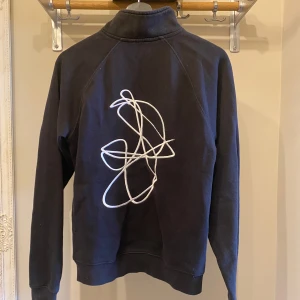 Tjocktröja med dragkedja från Poetic Collective - Svart tröja från Poetic Collective med halv dragkedja och ett abstrakt vitt broderat mönster på ryggen 🤍🖤