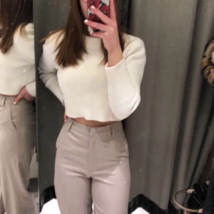 Vit croppad stickad tröja  - Säljer en stilren vit croppad stickad tröja med långa ärmar. Perfekt för en trendig look med hög midja. Tröjan har ribbade detaljer vid ärmslut och nederkant för extra stil. Enda defekten är att en tråd sticker ut på baksidan men det kan man lösa på något sätt. Den har inga hål eller andra skador. 