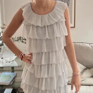Grå volangklänning - Säljer en söt grå klänning med flera lager av volanger. Klänningen har en rund halsringning, man kan också ha den ”snett” off shoulder på ena sidan. Perfekt för somriga dagar eller speciella tillfällen. 💫Volanger framtill.