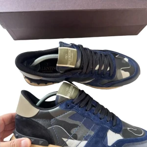Valentino Rockrunners - Snygga Valentino Rockrunner sneakers med ett coolt camouflagemönster i blått och beige. Skorna har svarta snören och en robust sula med bra grepp. Perfekta för en stilren och modern look. MVH scandicfashion 