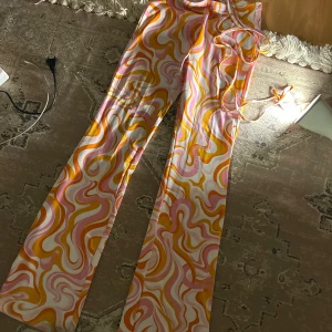 Mönstrade byxor  - Färgglada byxor från Divided med ett psykedeliskt mönster i rosa, orange och gult. Byxorna har en tight passform och är tillverkade i ett mjukt och stretchigt material. Perfekta för att sticka ut med en unik stil!