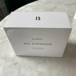 Byredo Bal D'Afrique Eau de Parfum 100ml - Säljer en elegant Byredo Bal D'Afrique Eau de Parfum i en stilren vit förpackning. Doften är känd för sina varma och exotiska noter, inspirerad av afrikansk kultur och konst. Perfekt för den som vill ha en unik och sofistikerad doftupplevelse.