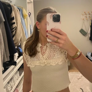 Beige topp med spetsdetaljer från Zara - Säljer en söt beige topp från Zara med spetsdetaljer och volang vid halsen. Toppen är ärmlös och har en ribbad nederdel som ger en fin passform. Sjukt söt och enkel att styla🥰💓💓