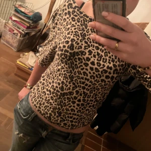 Leopardmönstrad offshoulder topp - Trendig leopardmönstrad topp med offshoulder-design. Perfekt för att ge en djärv touch till din outfit. Kortärmad och figurnära passform.