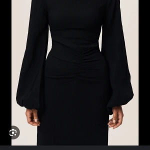 SÖKES!! Adoore Reno dress  - Elegant svart klänning med långa puffärmar och åtsittande passform. Klänningen har en smickrande rynkad detalj i midjan som framhäver figuren. Perfekt för en stilren look.