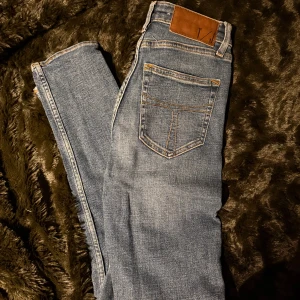 Blå jeans från Tiger of Sweden - Snygga blå jeans från Tiger of Sweden med klassisk femficksdesign och knappgylf. Perfekta för en stilren look. Märkeslapp i brunt läder 