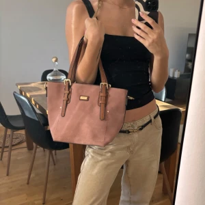 Väska - Rosa suede / mocka väska med bruna läderband. Har ett innerfack med dragkedja. Helt oanvänd. 