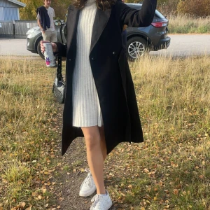 Vit ribbad stickad klänning - Mysig vit stickad klänning med ribbad struktur och långa ärmar. Perfekt för kyligare dagar med sin bekväma och stilrena design. Klänningen har en avslappnad passform som gör den lätt att bära.