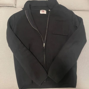 Overshirt - Säljer en svart tröja med dragkedja och en bröstficka. Tröjan har långa ärmar och en enkel design som passar till många tillfällen. Nypris 700kr