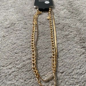 Guldhalsband från Ur&penn  - Snyggt guldhalsband från Montini med två olika kedjor. Perfekt för att lägga till en touch av elegans till din outfit. Halsbandet har en justerbar kedja för att passa olika längder.