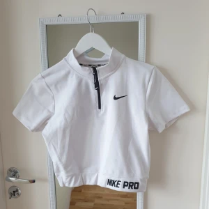 Kortärmad träningstopp Nike - Säljer en vitl kortärmad topp från Nike med dragkedja framtill och Dri-FIT teknologi. Perfekt för träning med en sportig look och bekväm passform. Nike-logga på bröstet och texten 'NIKE PRO' vid nederkanten. 🏋️‍♀️