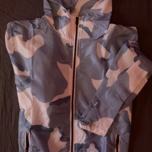 Cadenza windbreaker  med dragkedja - Säljer en Cadenza stilig windbreaker med blått och vitt camouflagemönster. Jackan har en praktisk dragkedja framtill och två fickor med dragkedjor. Perfekt för en cool och avslappnad look.